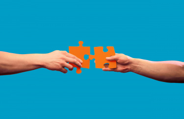 Zwei Hände von links und rechts mit jeweils einem Puzzleteil in der Hand