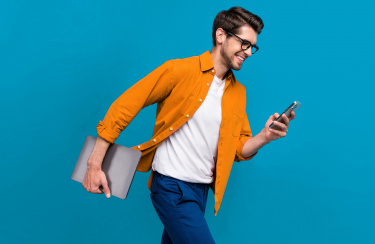 junger lässiger Mann geht zügig und schaut dabei auf sein Handy