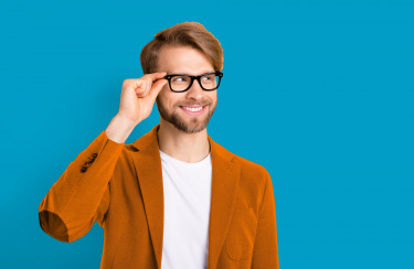 Mann fasst sich an seine Brille und schaut lächelnd zur Seite