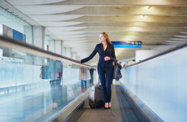 Junge elegante Geschäftsfrau mit Handgepäck auf Reisenden am internationalen Flughafen Terminal. Flugbegleiter mit Koffer.