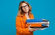 Frau mit Brille schaut genervt mit einem Stapel Ordnern in der Hand