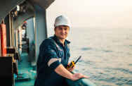 Ein lächelnder Mann steht auf einem Schiff und hält ein Funkgerät in der Hand