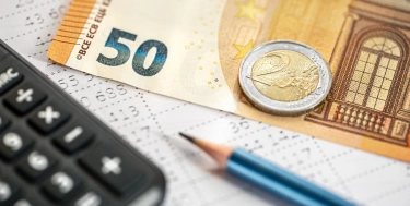 Nahaufnahme von Taschenrechner, Geldscheinen und Bleistift vor verschwommenem Hintergrund