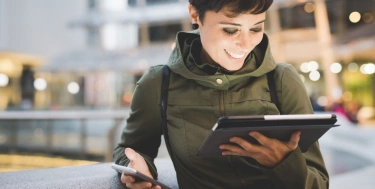 junge frau schaut auf ihr Tablet und hält ein Smartphone in der anderen Hand
