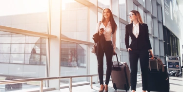 Zwei lächelnde Geschäftspartner gehen mit Koffern auf Geschäftsreise und gehen durch den Flughafengang