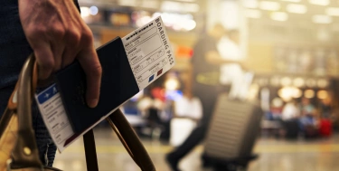 Ein Mann im Flughafen hält eine Tasche und sein Flugticket in der Hand.