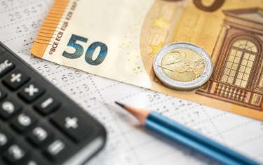 Nahaufnahme von Taschenrechner, Geldscheinen und Bleistift vor verschwommenem Hintergrund