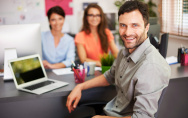 3 Personen sitzen im Büro am Schreibtisch fröhlich lächelnd