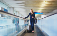 Junge elegante Geschäftsfrau mit Handgepäck auf Reisenden am internationalen Flughafen Terminal. Flugbegleiter mit Koffer.