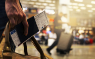 Ein Mann im Flughafen hält eine Tasche und sein Flugticket in der Hand.