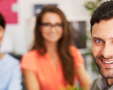 3 Personen sitzen im Büro am Schreibtisch fröhlich lächelnd